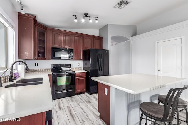 kitchen with sink, light hardwood / wood-style flooring, a kitchen bar, a kitchen island, and black appliances