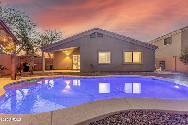 pool at dusk featuring ceiling fan and a patio