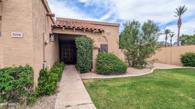 property entrance featuring a yard, fence, a tile roof, and stucco siding