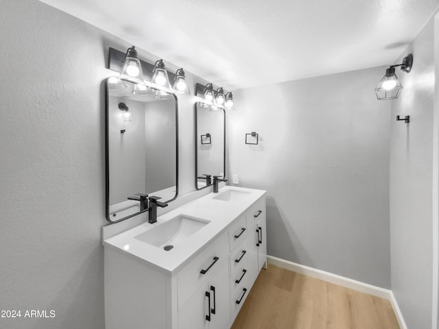 bathroom with double vanity, wood finished floors, a sink, and baseboards