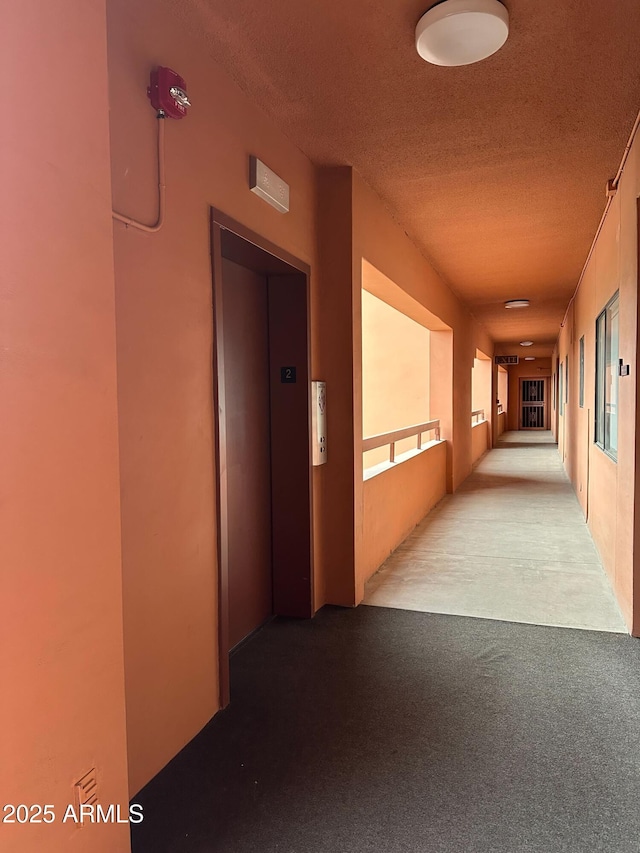 hallway with elevator, carpet flooring, and a textured ceiling