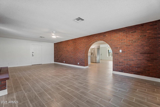 unfurnished living room featuring wood-type flooring, brick wall, and a textured ceiling