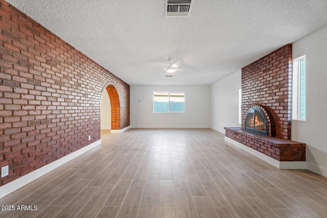 unfurnished living room with a brick fireplace, a textured ceiling, ceiling fan, and brick wall