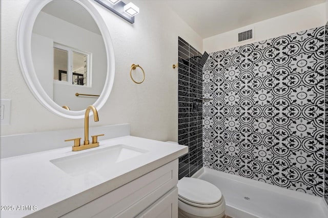 bathroom with vanity, toilet, and a tile shower