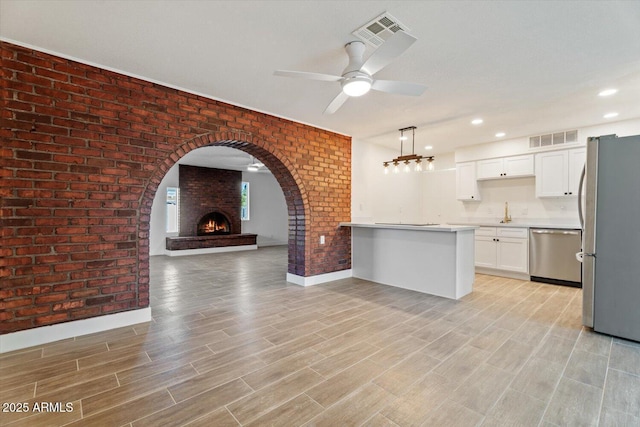 kitchen featuring pendant lighting, ceiling fan, appliances with stainless steel finishes, white cabinetry, and brick wall