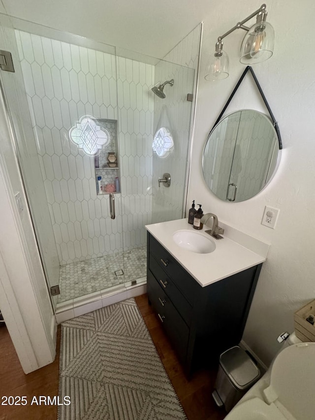 bathroom featuring toilet, a stall shower, wood finished floors, and vanity