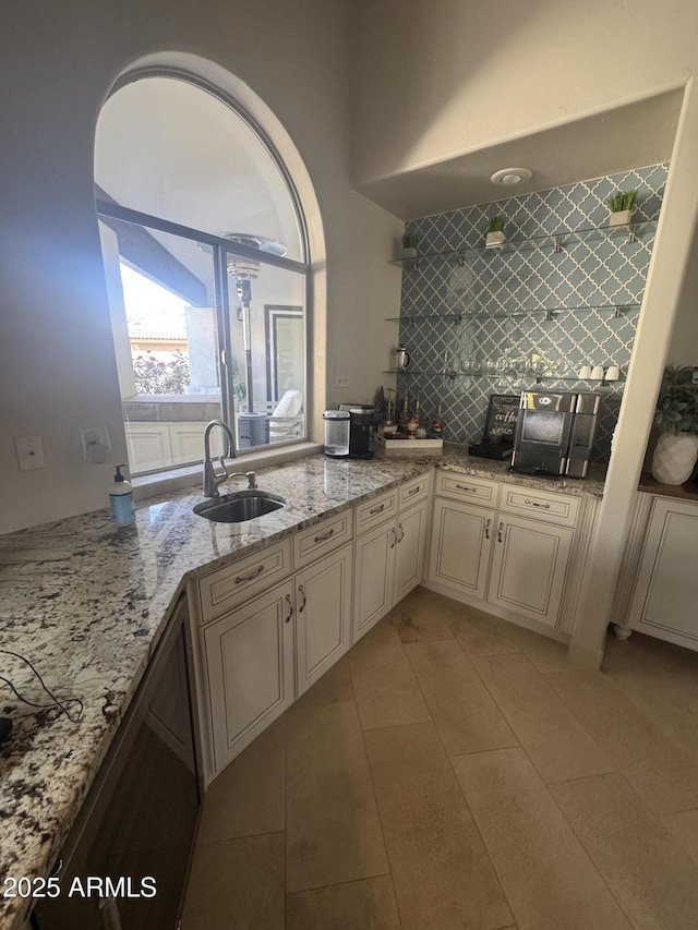 kitchen with light stone counters, light tile patterned floors, backsplash, a sink, and cream cabinetry