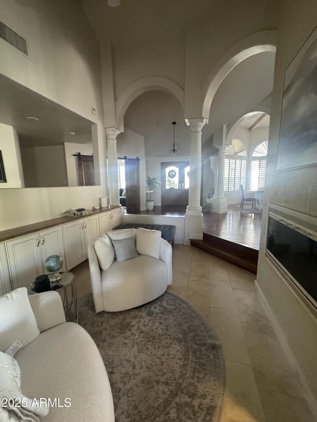 living area with light tile patterned flooring, arched walkways, visible vents, and decorative columns