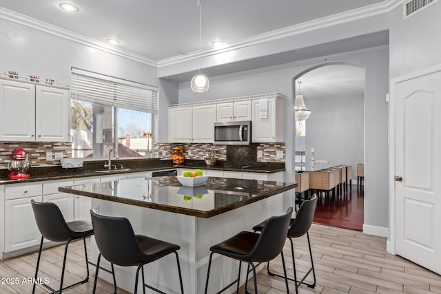 1442 W Laurel Ave, Gilbert, AZ 85233 - kitchen featuring stainless steel microwave, ornamental molding, a breakfast bar area, white cabinets, and backsplash