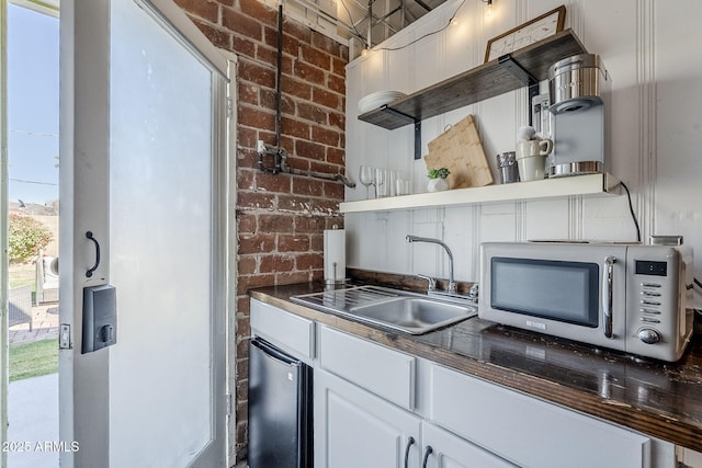 kitchen featuring brick wall, sink, and white cabinets