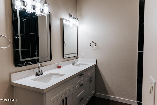 full bath with double vanity, a textured wall, baseboards, and a sink