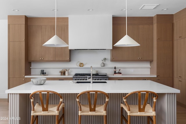 kitchen with sink, light hardwood / wood-style floors, hanging light fixtures, and a kitchen island with sink