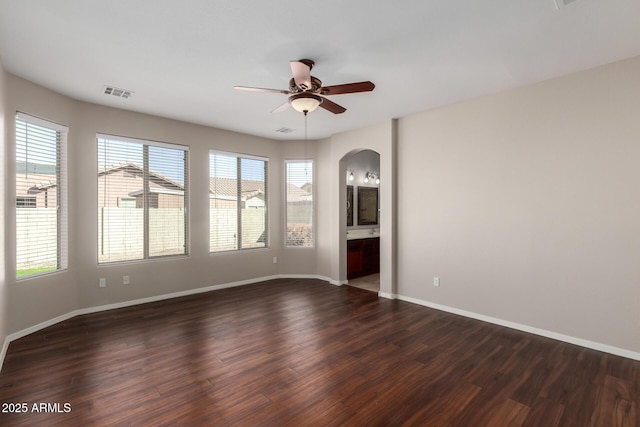 unfurnished room featuring baseboards, visible vents, arched walkways, ceiling fan, and dark wood-style flooring