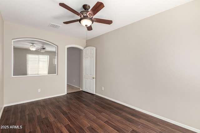 spare room featuring arched walkways, dark wood-style flooring, visible vents, ceiling fan, and baseboards