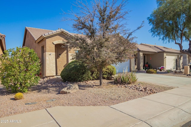 view of front of property featuring an attached garage, a tiled roof, concrete driveway, and stucco siding