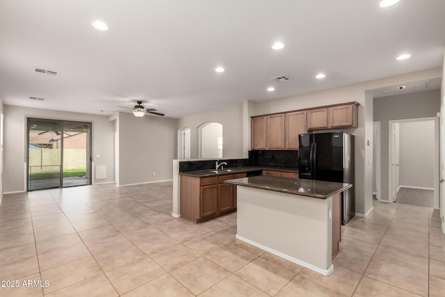 kitchen with tasteful backsplash, arched walkways, a ceiling fan, a kitchen island, and dark stone countertops