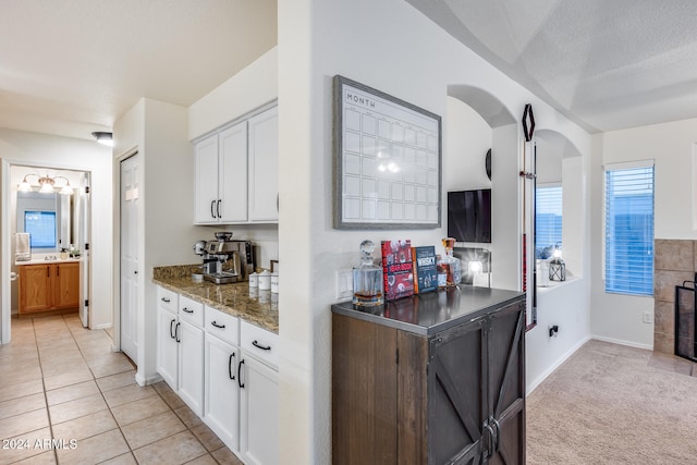 kitchen featuring white cabinetry, a textured ceiling, dark stone counters, and light tile patterned floors