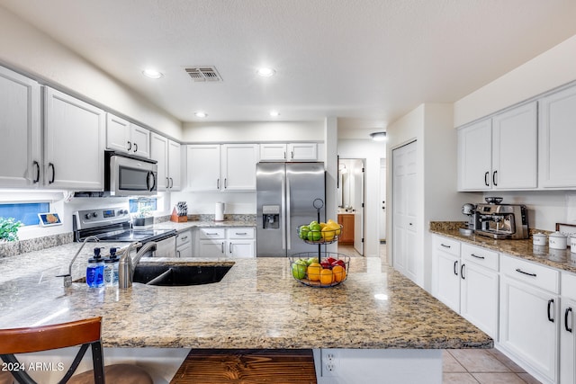 kitchen with white cabinetry, light stone counters, a kitchen bar, and stainless steel appliances