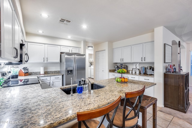 kitchen featuring kitchen peninsula, stove, a breakfast bar area, stainless steel fridge with ice dispenser, and washing machine and clothes dryer