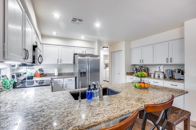 kitchen featuring stainless steel appliances, white cabinetry, sink, light stone countertops, and a kitchen bar