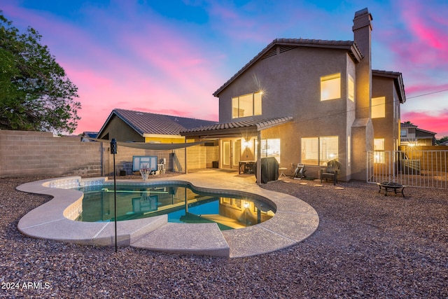 back house at dusk featuring a fenced in pool and a patio area