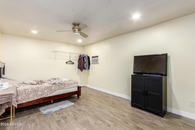 bedroom with a wall mounted AC, ceiling fan, and light hardwood / wood-style floors