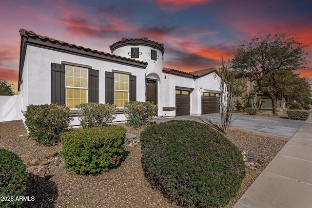 mediterranean / spanish-style home featuring a tiled roof, a garage, driveway, and stucco siding