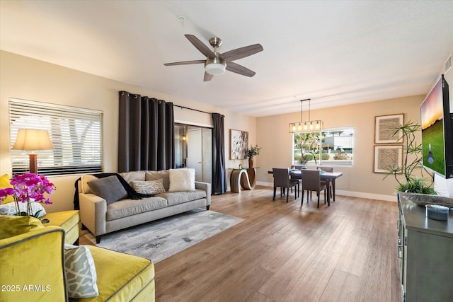 living room featuring ceiling fan with notable chandelier, baseboards, light wood-style flooring, and a healthy amount of sunlight