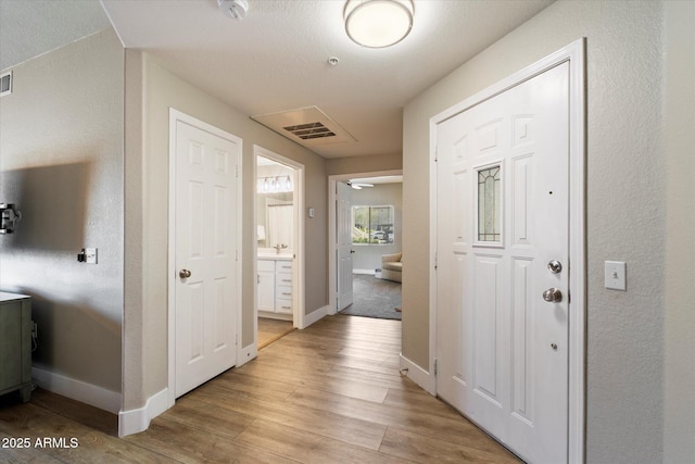 hall featuring light wood finished floors, visible vents, and baseboards