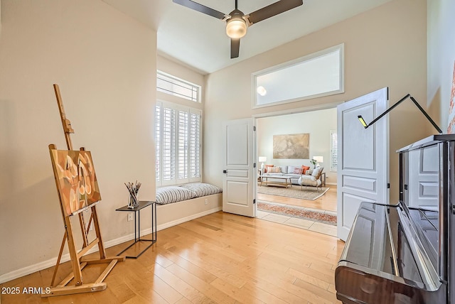 living area with baseboards, ceiling fan, a towering ceiling, and light wood finished floors