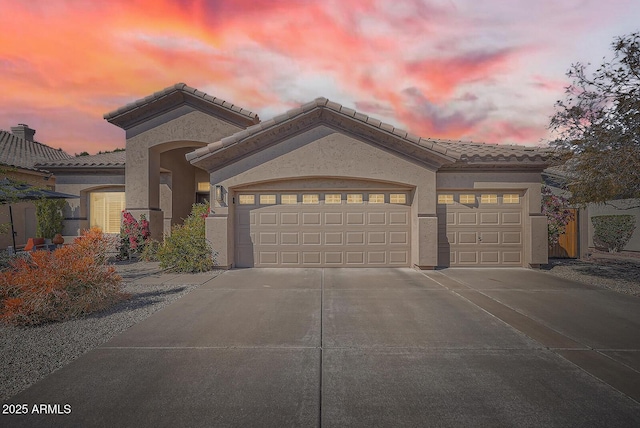 mediterranean / spanish-style house featuring stucco siding, a garage, driveway, and a tile roof