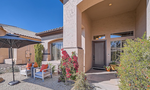 view of exterior entry with a tiled roof, stucco siding, and a patio area