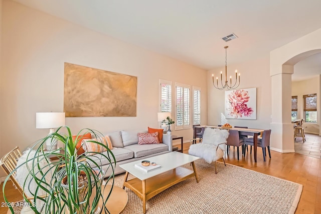 living area featuring visible vents, arched walkways, light wood-style floors, baseboards, and a chandelier