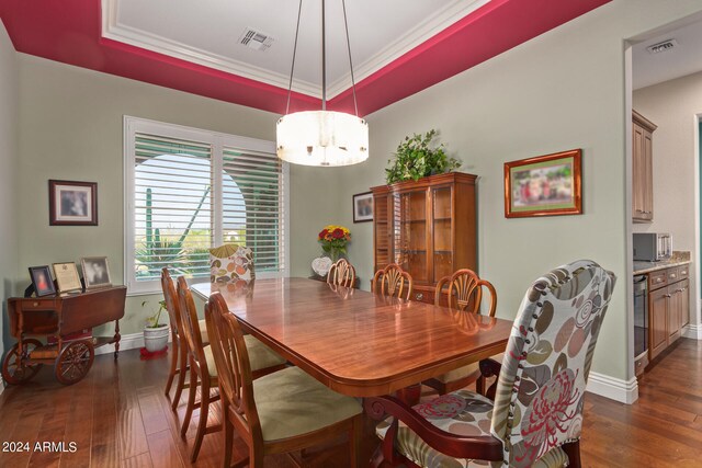 dining room with ornamental molding, a raised ceiling, an inviting chandelier, and dark hardwood / wood-style flooring