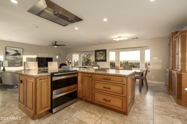 kitchen with light stone counters, electric range, wall chimney exhaust hood, and a kitchen island