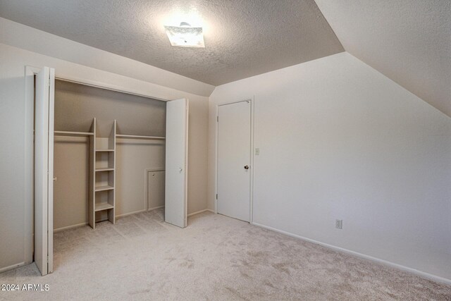 unfurnished bedroom with light carpet, a closet, a textured ceiling, and vaulted ceiling