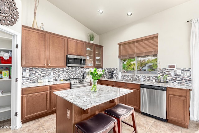 kitchen with sink, backsplash, lofted ceiling, a kitchen island, and appliances with stainless steel finishes