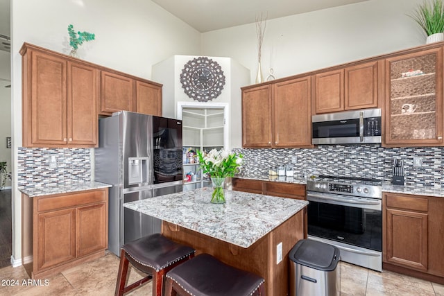 kitchen with a center island, tasteful backsplash, light stone counters, a kitchen bar, and appliances with stainless steel finishes