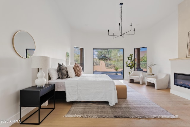 24645 N 117th St, Scottsdale, AZ 85255 - bedroom featuring a chandelier, wood finished floors, a glass covered fireplace, access to outside, and a towering ceiling