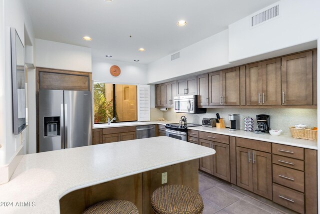 kitchen with sink, decorative backsplash, appliances with stainless steel finishes, light tile patterned flooring, and a breakfast bar area