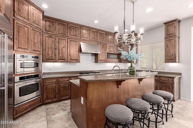 kitchen featuring wall chimney range hood, gas cooktop, stainless steel built in fridge, a breakfast bar, and a chandelier