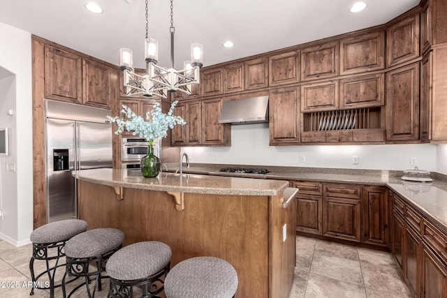 kitchen featuring built in refrigerator, black gas cooktop, a chandelier, range hood, and a center island with sink