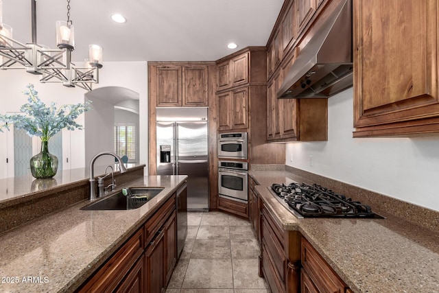 kitchen featuring under cabinet range hood, a sink, appliances with stainless steel finishes, arched walkways, and dark stone counters
