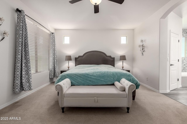 carpeted bedroom featuring arched walkways, baseboards, multiple windows, and a ceiling fan