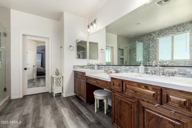 ensuite bathroom with wood finished floors, a stall shower, double vanity, and tasteful backsplash