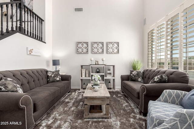 living room with a towering ceiling, dark colored carpet, and baseboards
