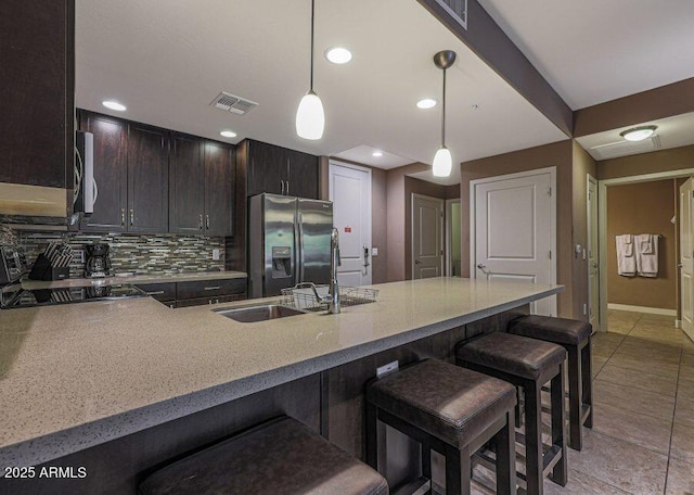 kitchen with pendant lighting, backsplash, a kitchen breakfast bar, stainless steel fridge, and dark brown cabinets