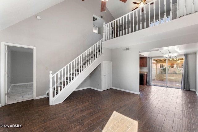 unfurnished living room featuring dark wood-type flooring, high vaulted ceiling, and ceiling fan with notable chandelier