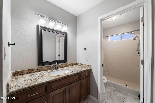 bathroom featuring a tile shower, vanity, and toilet