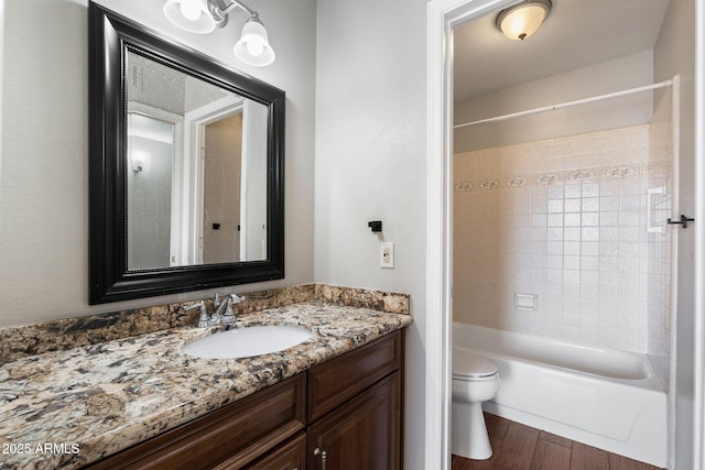 full bathroom with hardwood / wood-style flooring, tiled shower / bath, vanity, and toilet